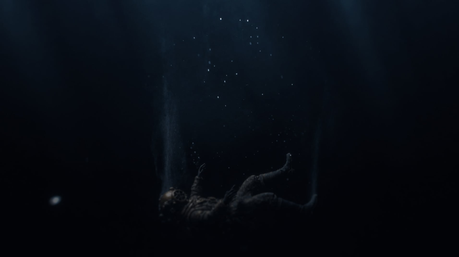 A diver in a brass helmet drifts through dark water as bubbles rise.